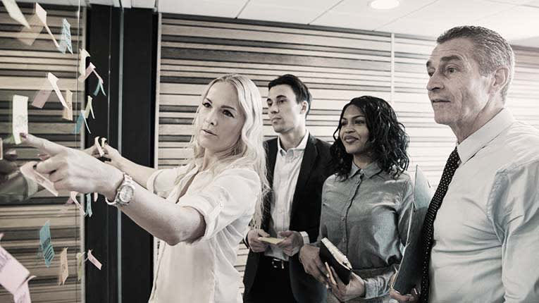 A group of business people standing in front of a wall with sticky notes.