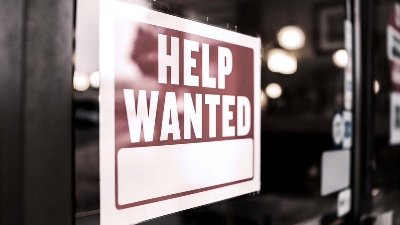 A sign that says help wanted on a glass door.