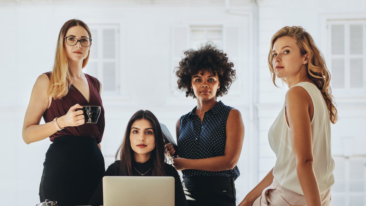 A group of business women standing around a table with laptops.