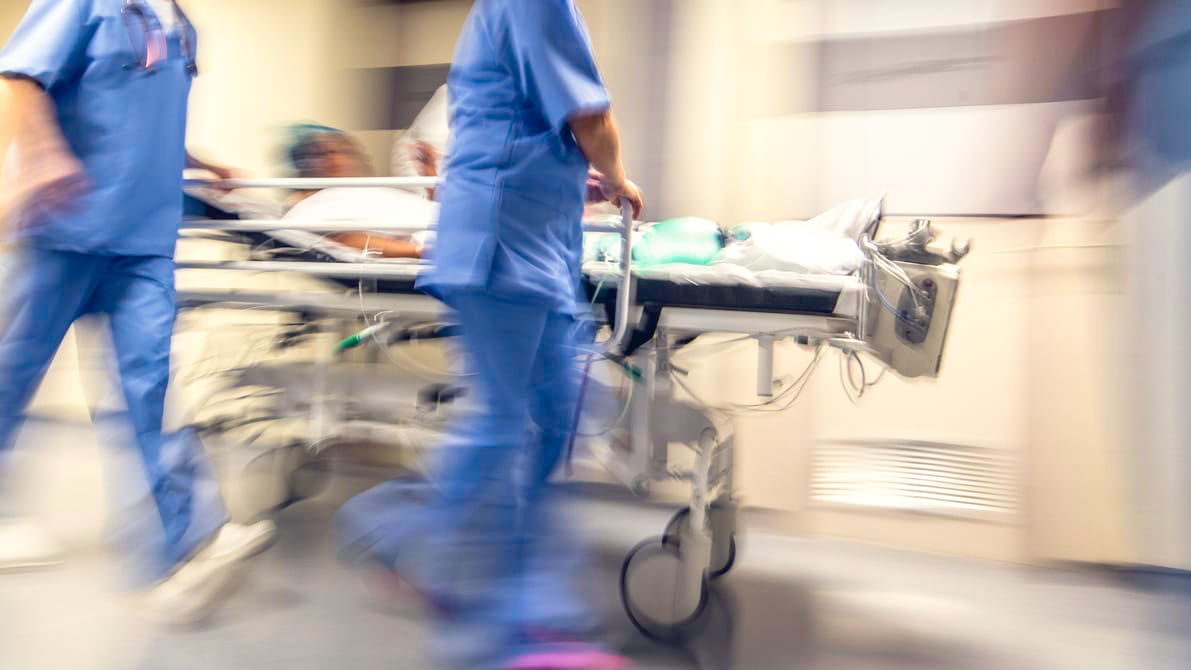 A blurry image of a group of hospital workers pushing a patient on a stretcher.