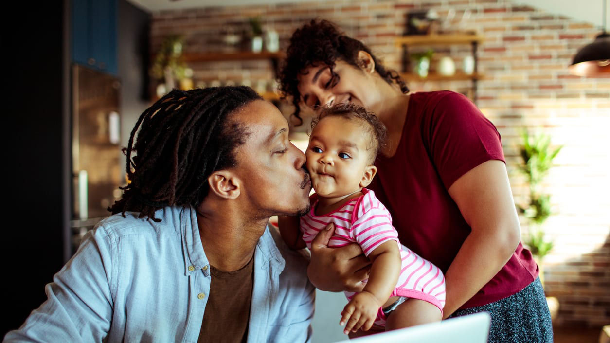 A man and woman kissing a baby in front of a laptop.