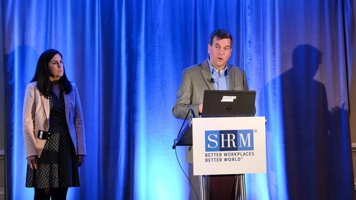 Two people standing at a podium with a laptop in front of them.