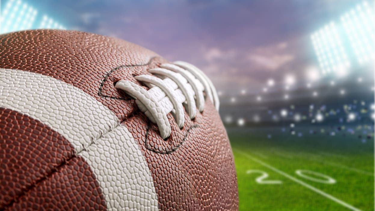 A football on a field with a stadium in the background.