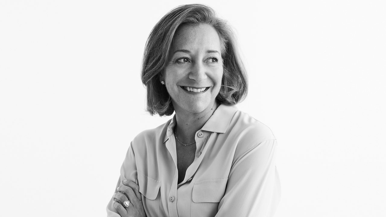 A woman with her arms crossed is smiling in a black and white photo.