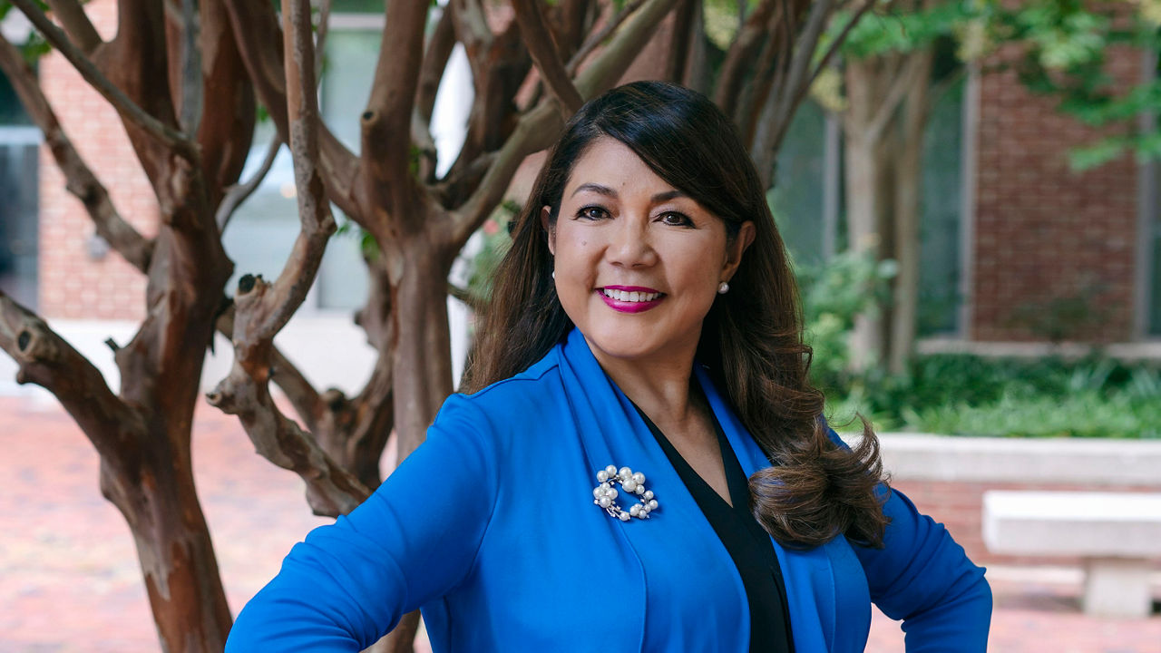 A woman in a blue jacket standing in front of a tree.