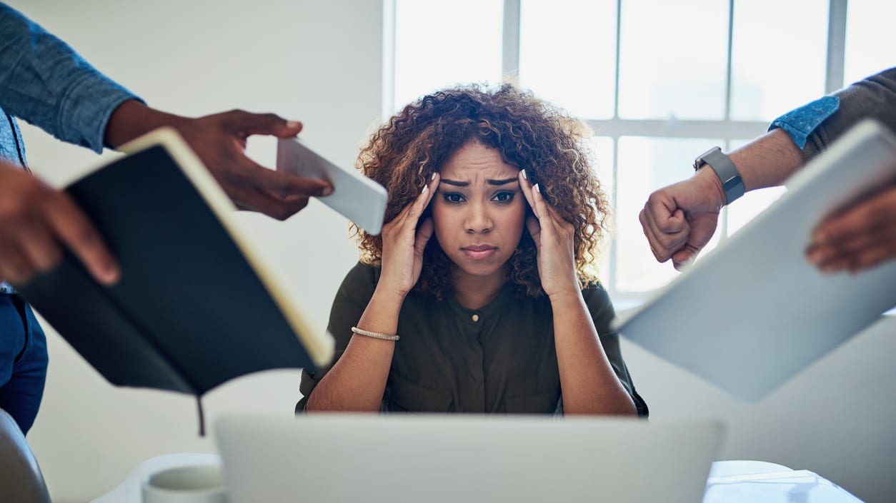 A woman looking stressed while a group of people surround her competing for her attention.