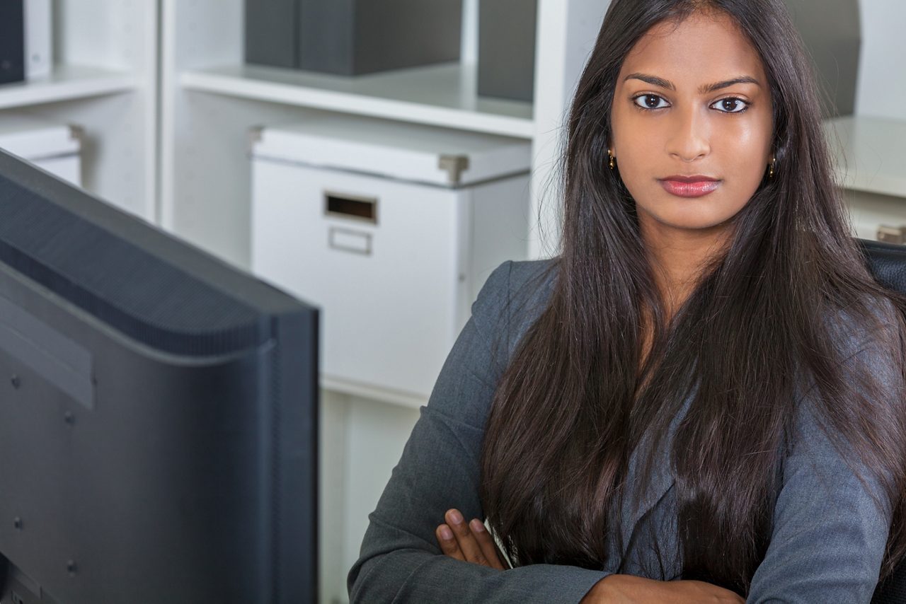 Businesswoman seated at her computer with arms crossed