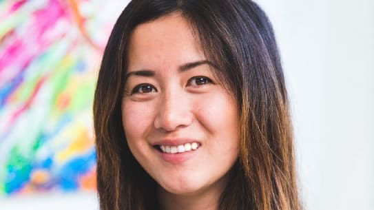An woman smiling in front of a colorful painting.
