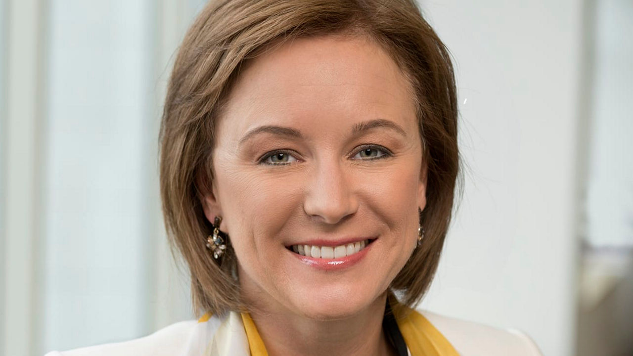 A smiling woman wearing a yellow and white scarf.
