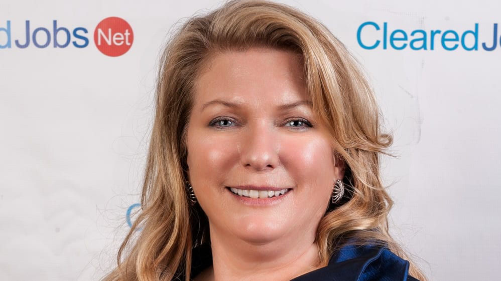 A woman in a blue dress standing in front of a clearjobs banner.