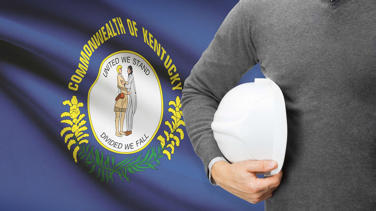A man holding a hard hat in front of the kentucky flag.