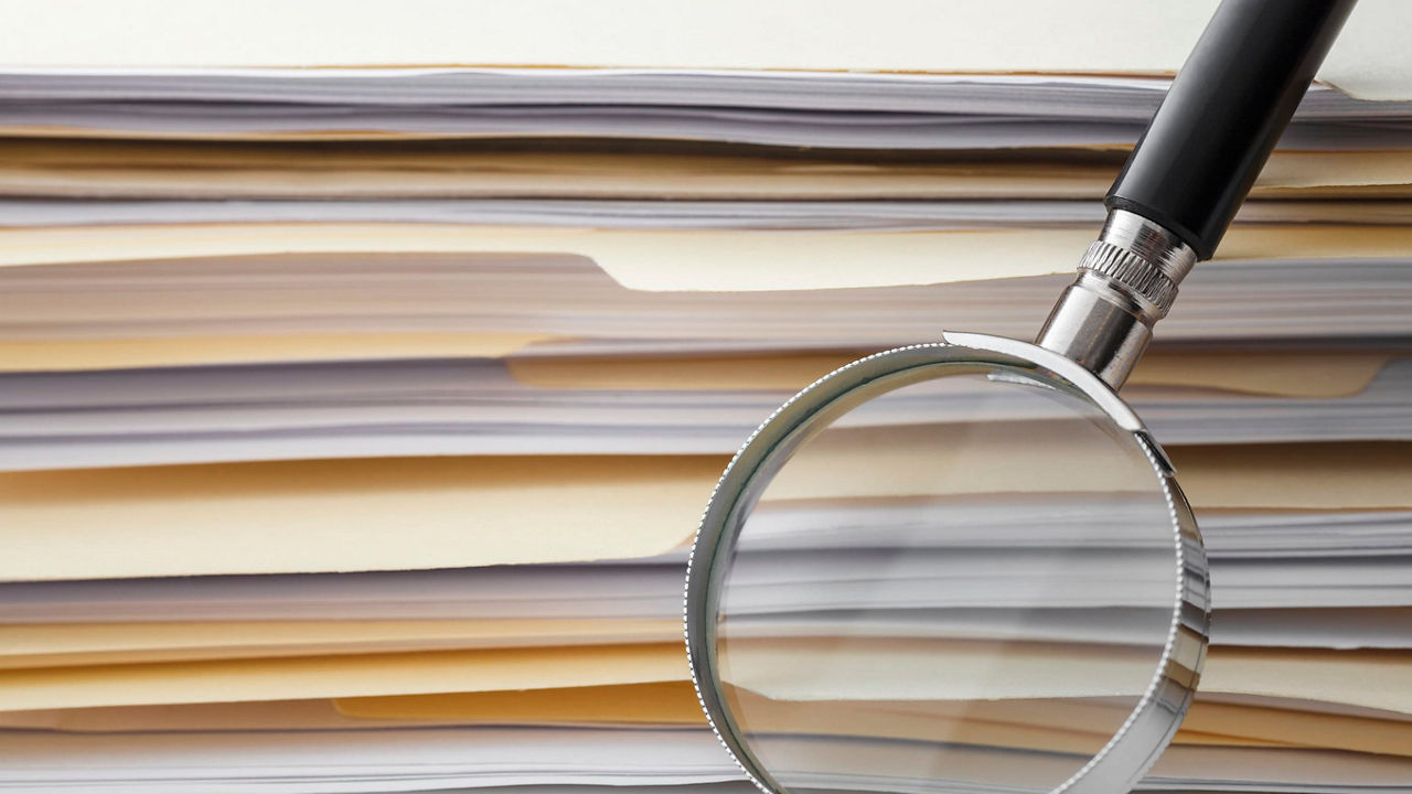 A magnifying glass on top of a pile of documents.