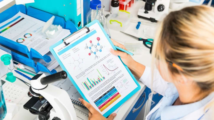 A woman in a lab coat is looking at a clipboard.