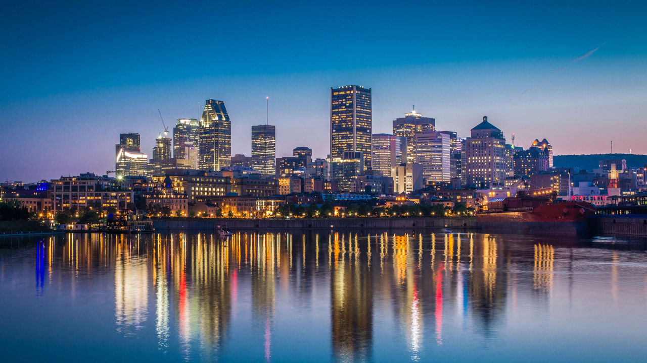 A city skyline is reflected in the water at dusk.