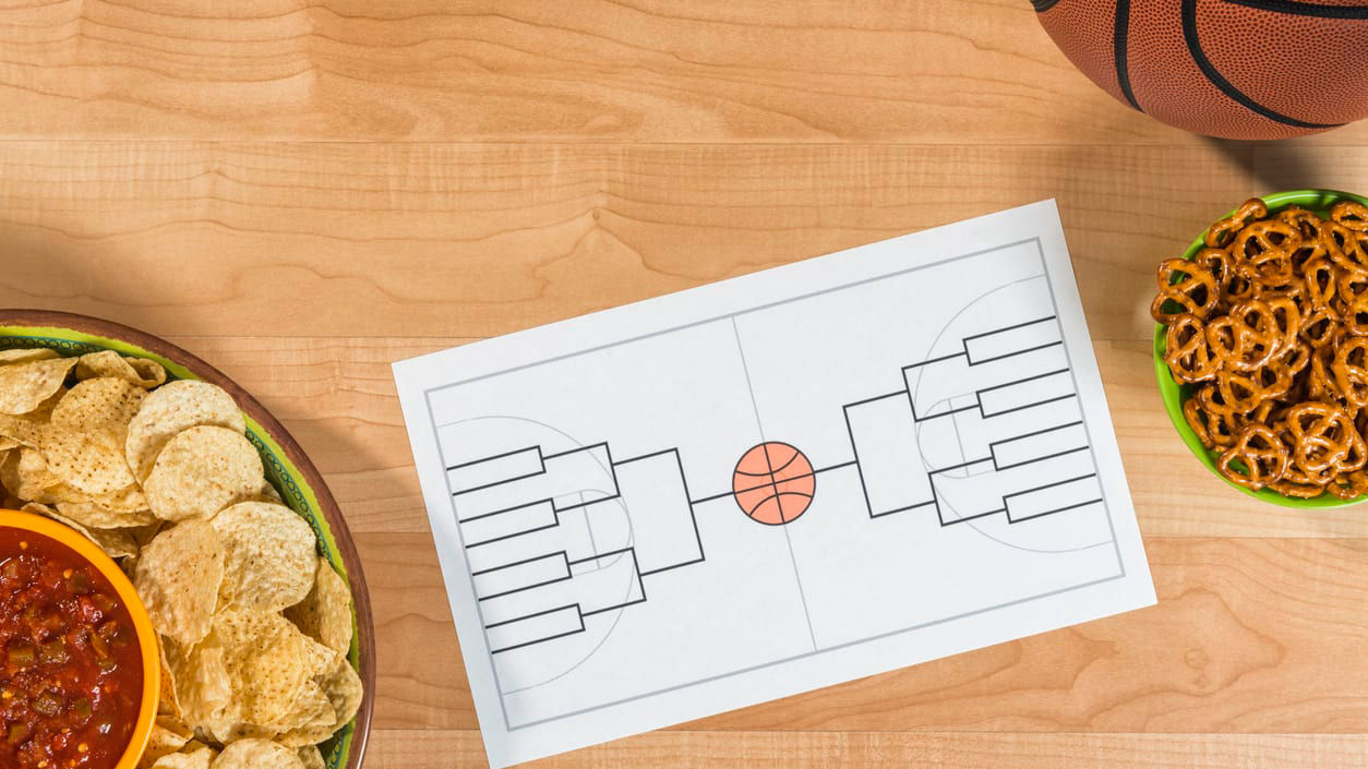 A bowl of chips, a basketball, and a basketball bracket on a table.