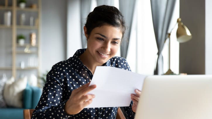 A woman sitting at a desk with a laptop holding a letter.