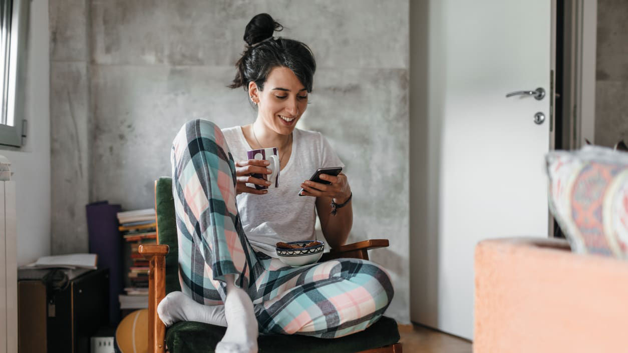 A woman in pajamas sitting in a chair and using her phone.