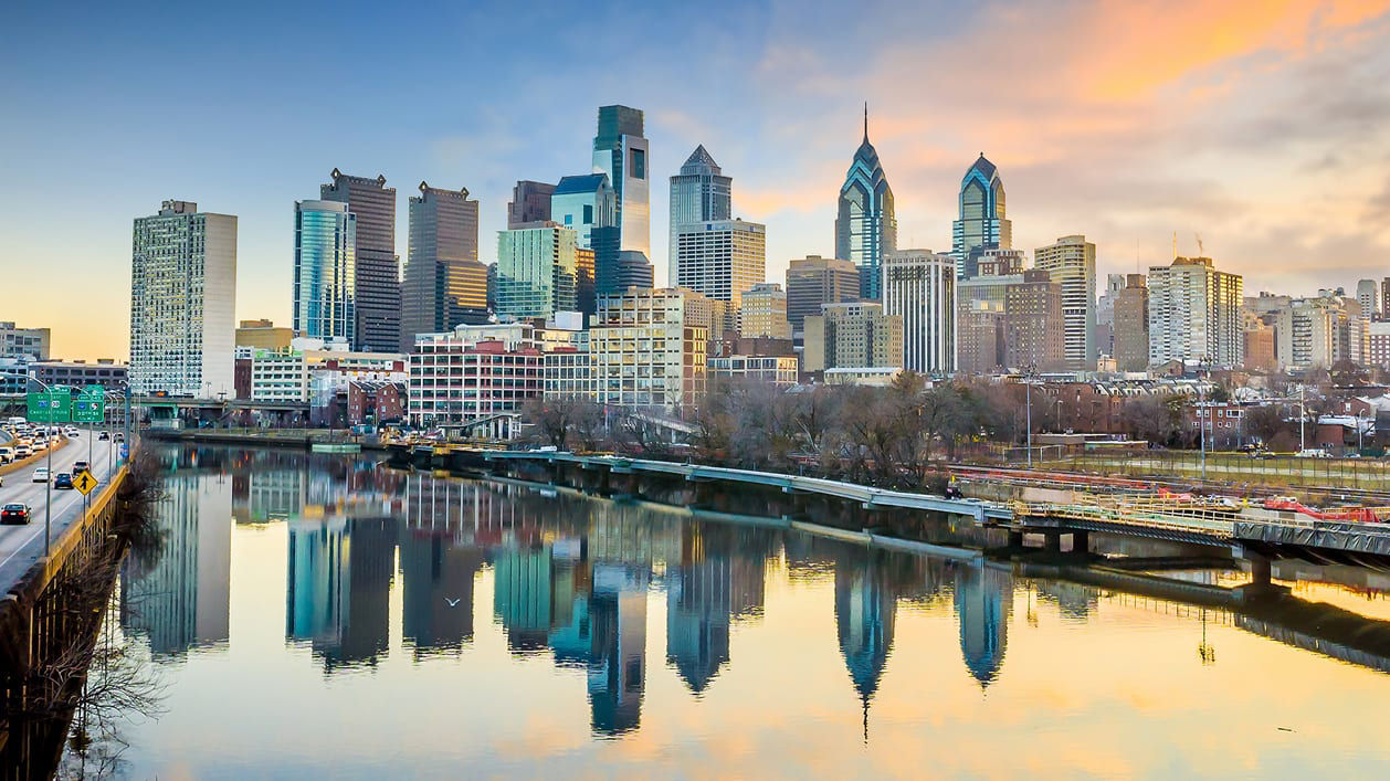 The skyline of philadelphia is reflected in a river.
