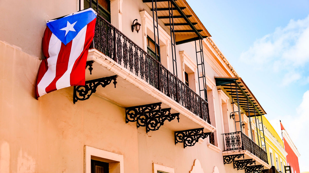 A puerto rican flag hangs from the balcony of a building.