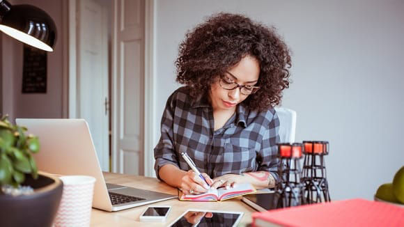 A woman sitting at a desk with a laptop and a notebook.