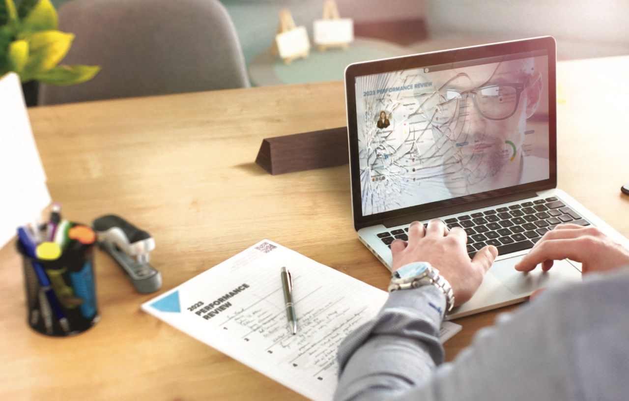 man typing on a laptop with broken screen and performance review paperwork next to him