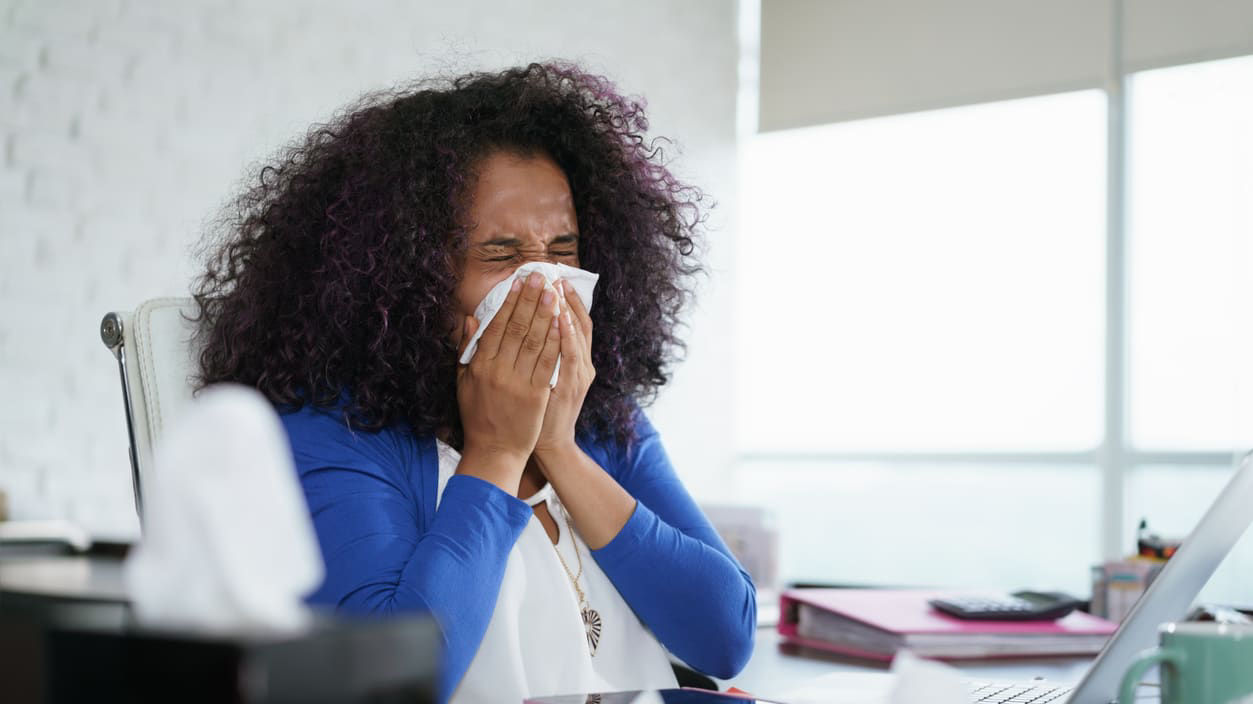 A woman blowing her nose in front of a laptop.