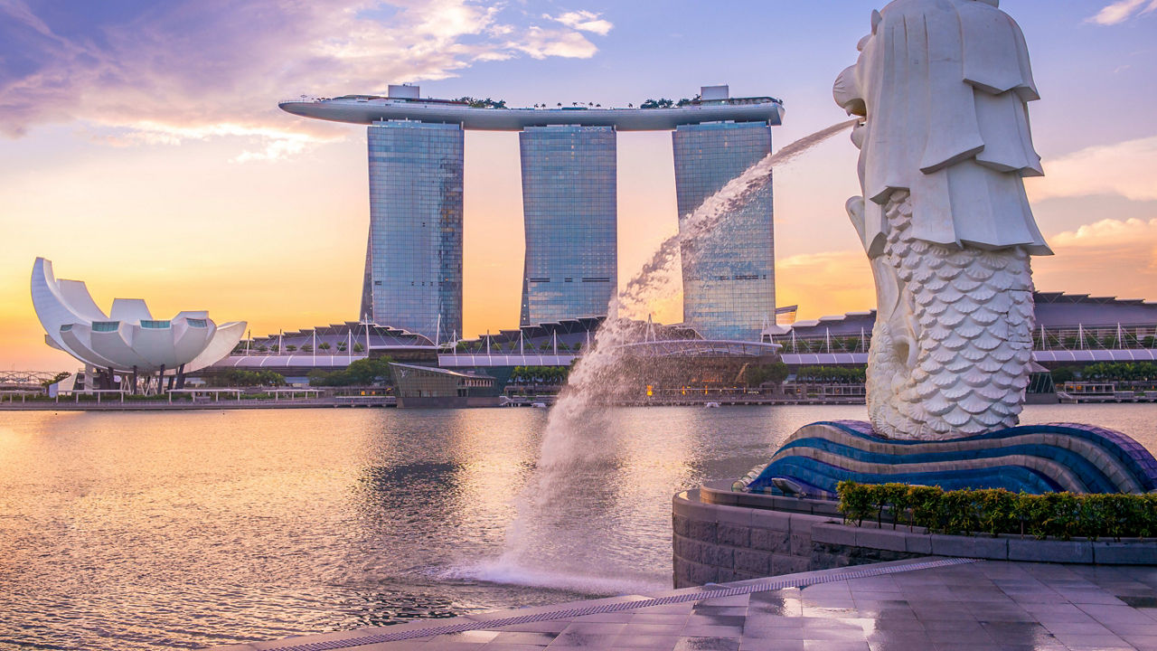 A modern skyscraper in Singapore in the background with a sculpture in the foreground and body of water between