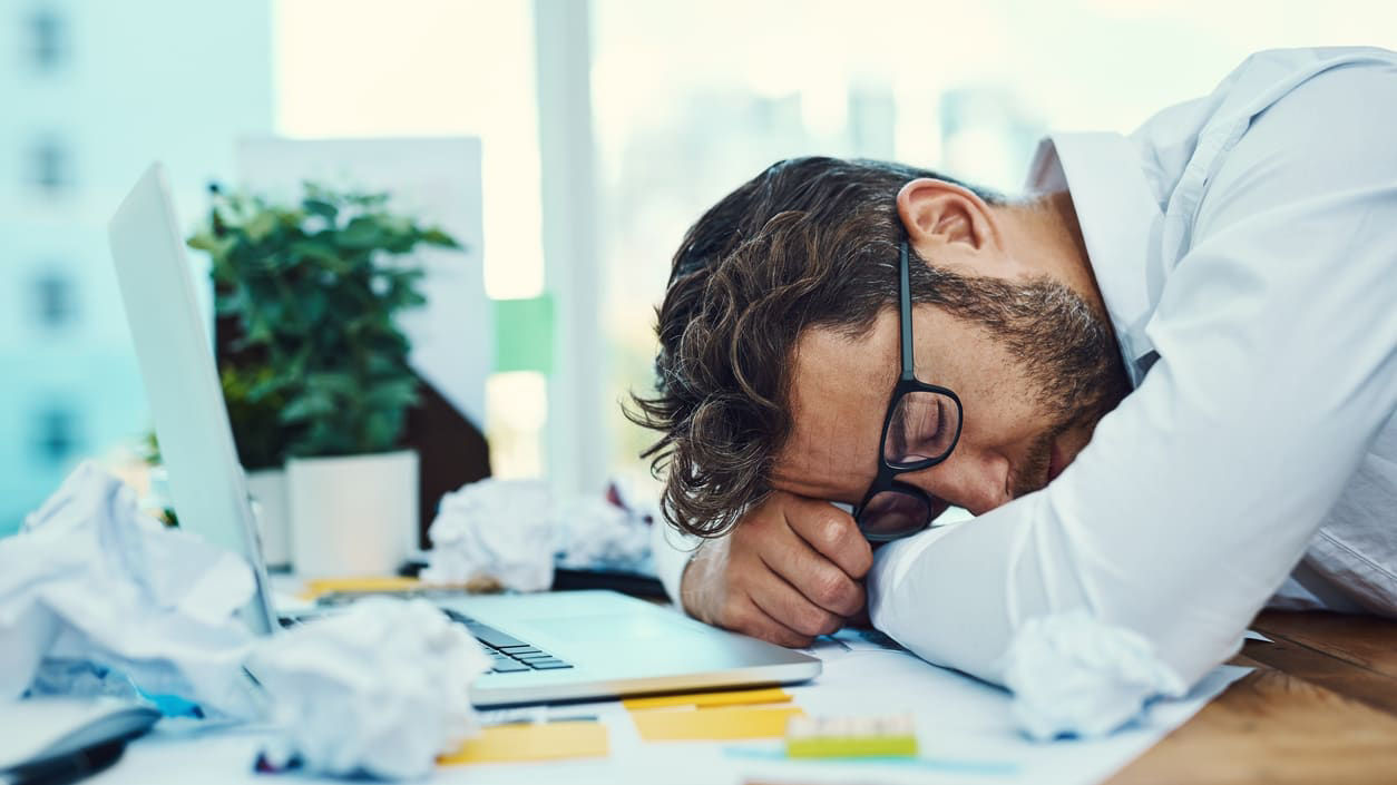 A man is sleeping on a desk with a laptop.