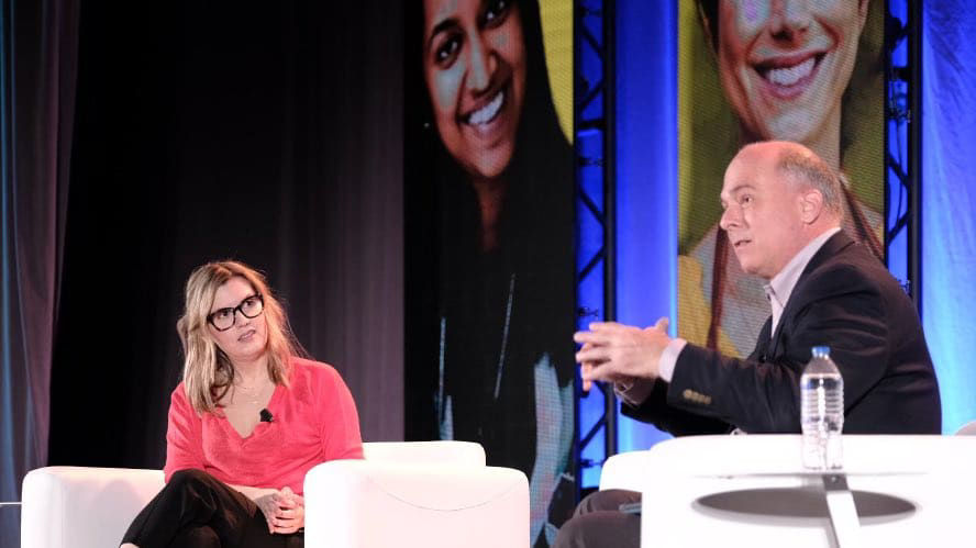 A man and woman talking on stage at a conference.