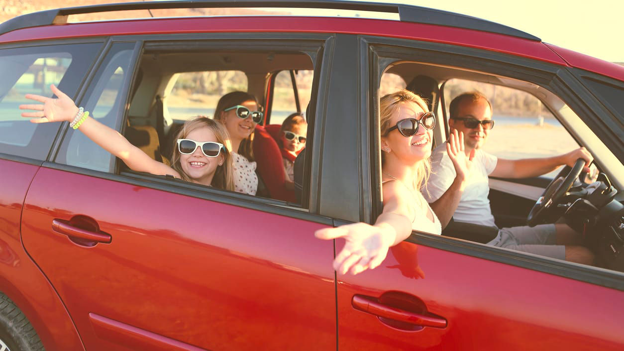 A group of people in a red car waving.