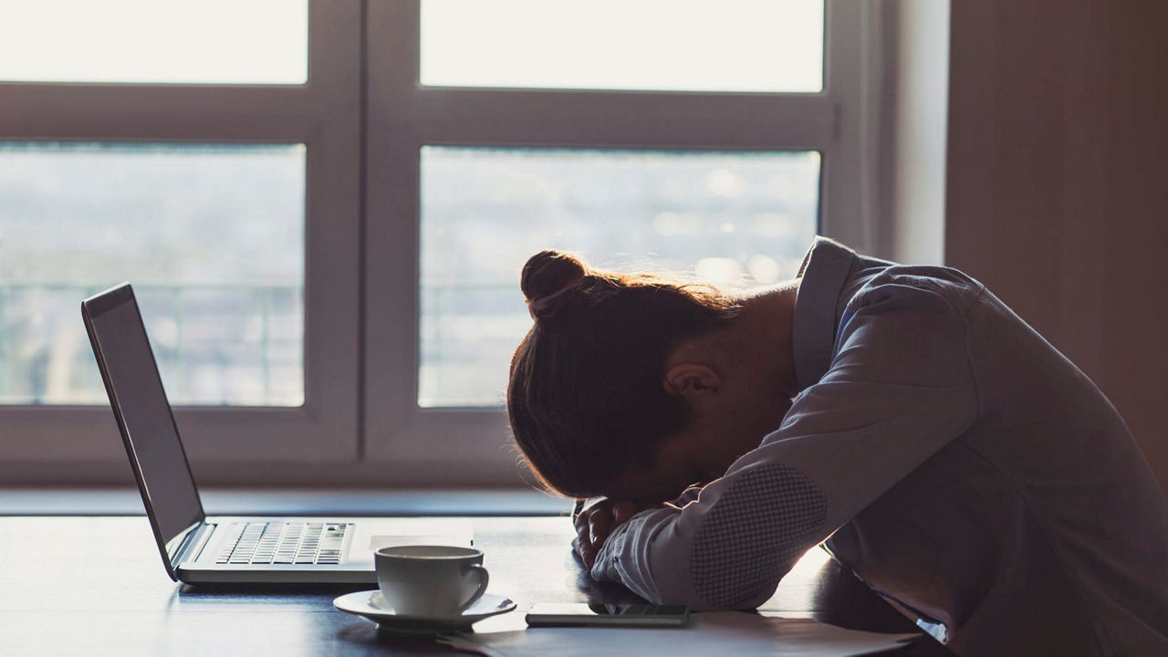 A woman is sitting at a desk with a laptop and a cup of coffee.