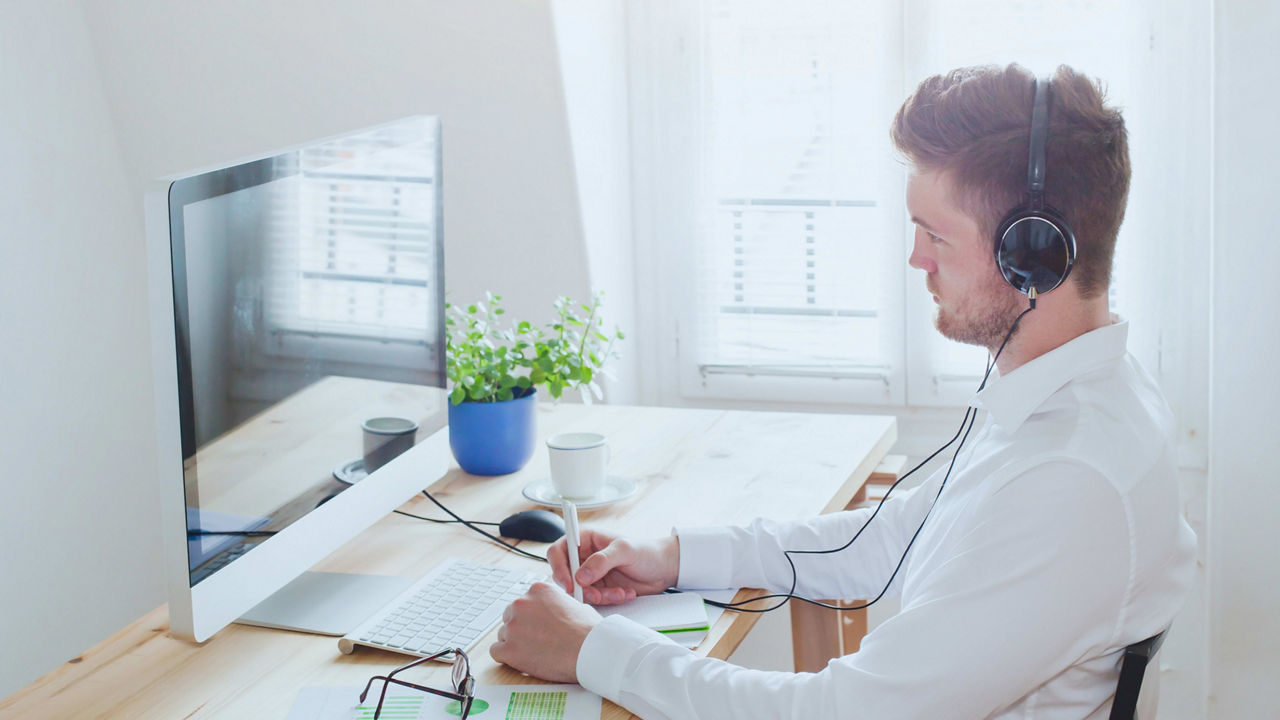 A man in a white shirt is wearing a headset and sitting at a desk.