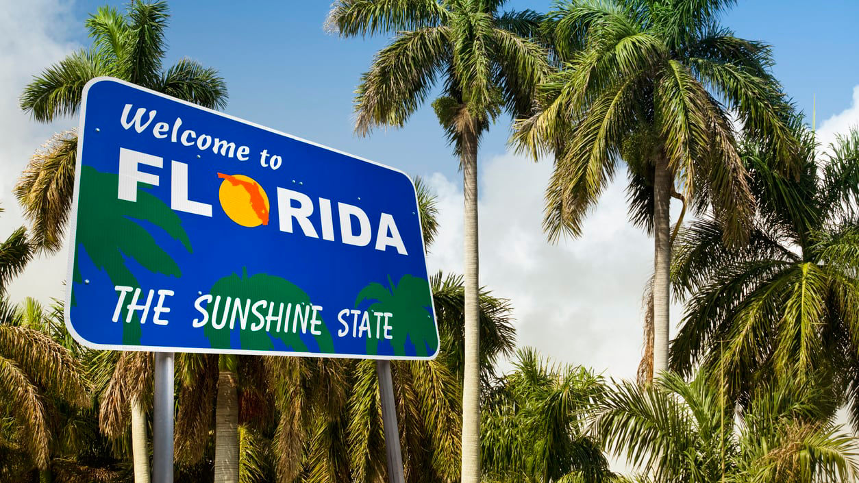 A welcome to florida sign in front of palm trees.