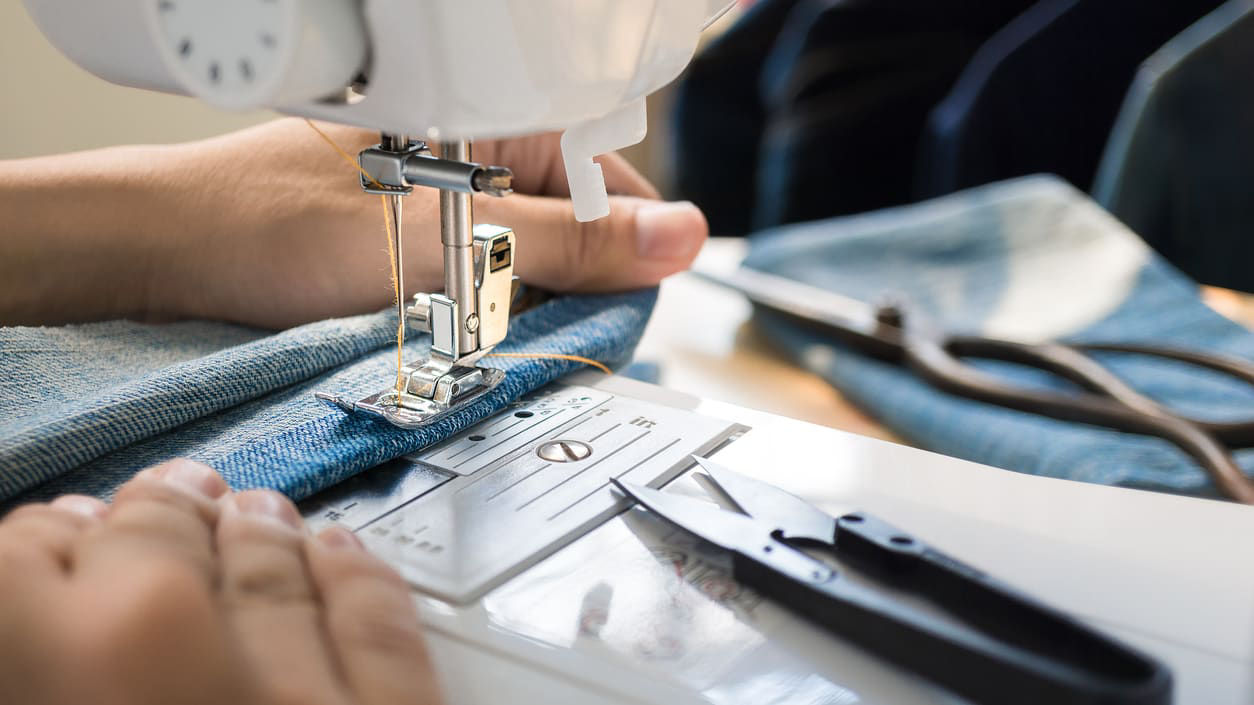 A person using a sewing machine to sew a pair of jeans.