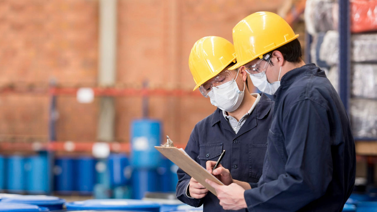 Two workers in hard hats looking at a clipboard in a warehouse.