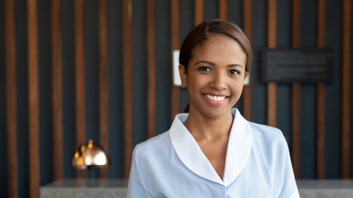 A smiling woman in a blue uniform standing in front of a reception desk.