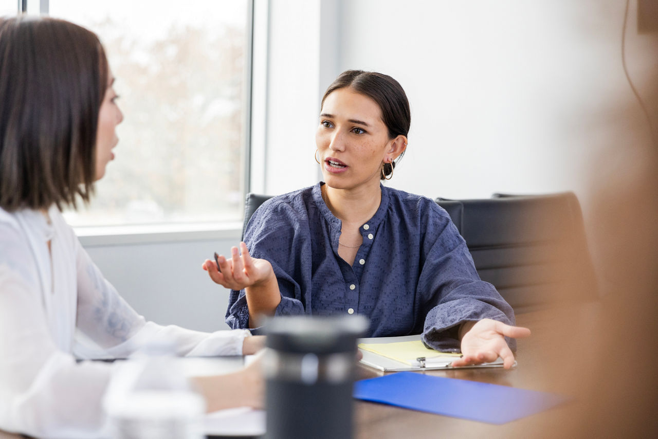 A young adult female employee puts her hands out in refusing a request from her female manager.