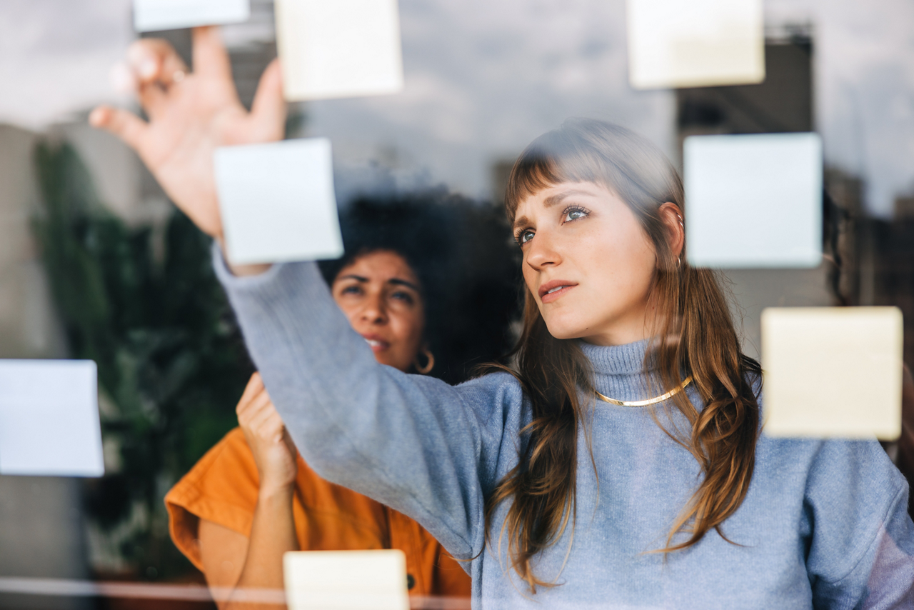 Creative businesswomen brainstorming using sticky notes. Young businesswomen discussing their business ideas during a meeting. Two female entrepreneurs working as a team in a modern office.