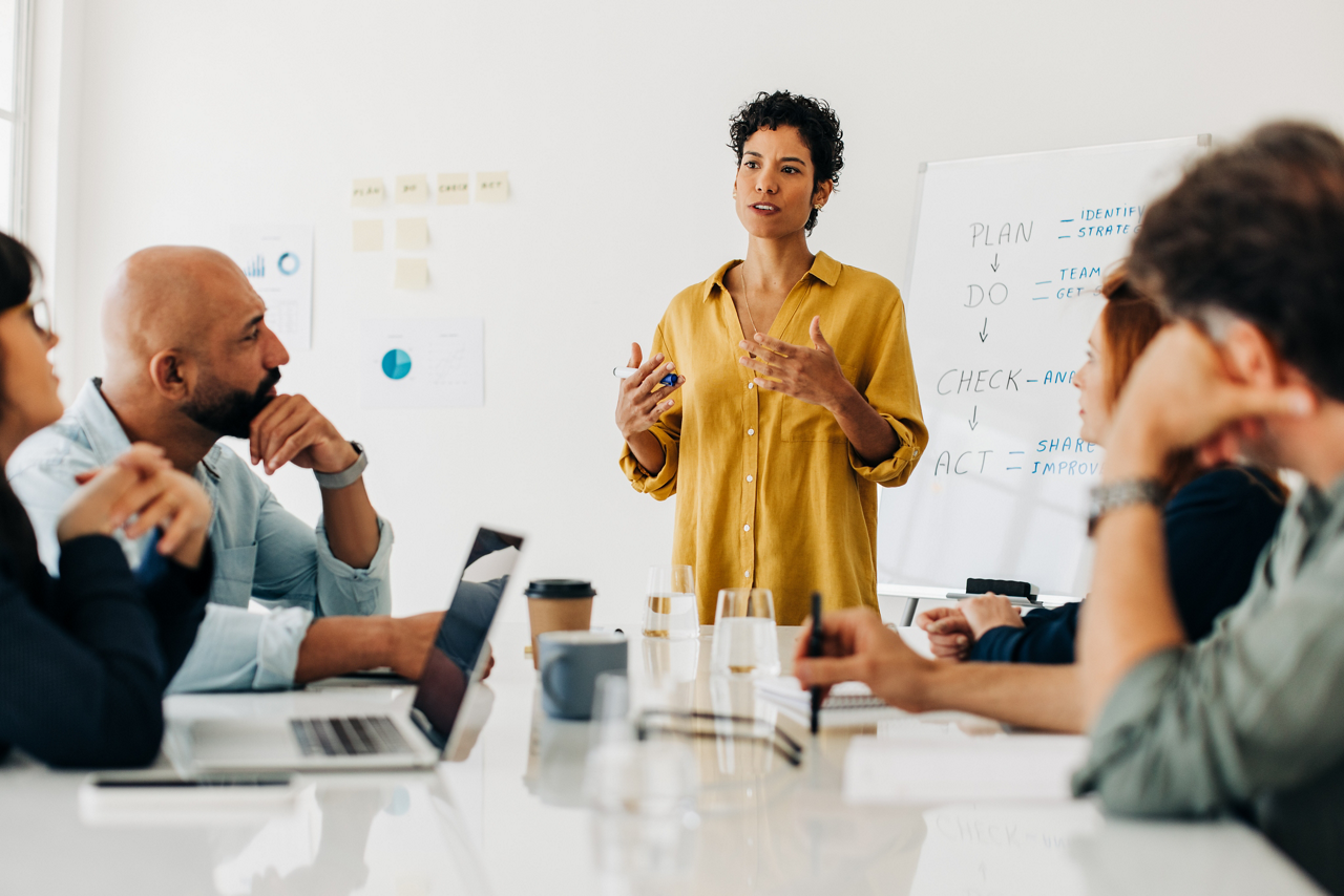 Business woman giving a speech during a boardroom meeting. Professional woman having a discussion with her colleagues in an office. Female project manager leading her team.