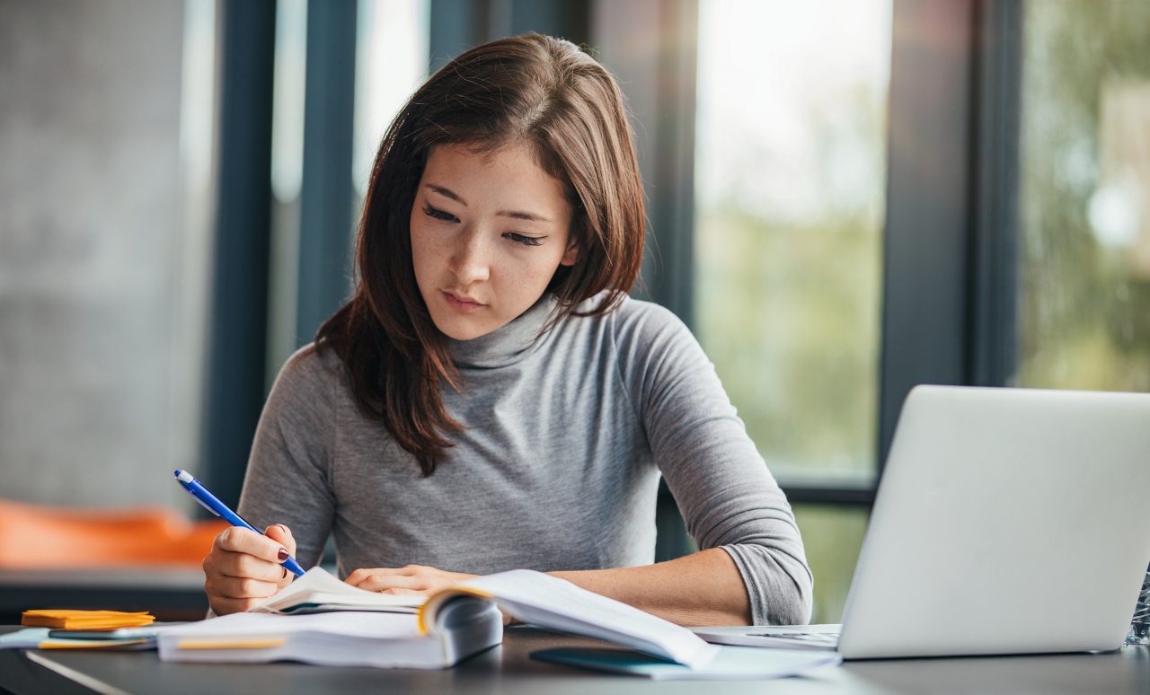 Woman studies with laptop, textbook