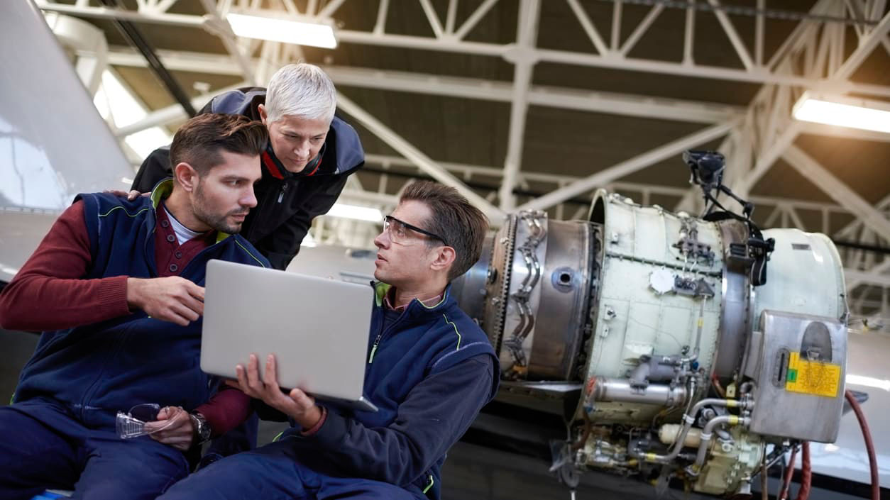 Three men looking at a laptop in a factory.