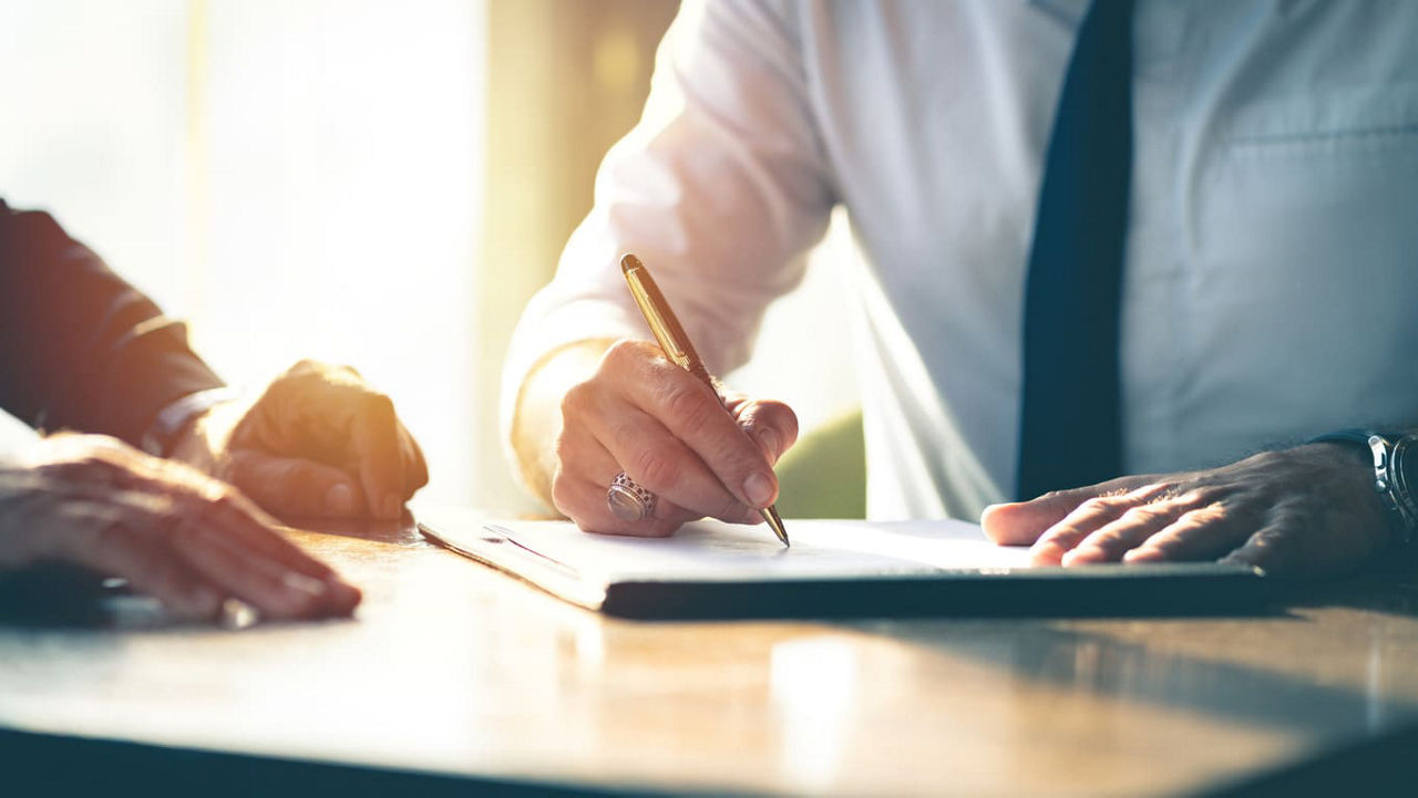 Two businessmen signing a document at a table.
