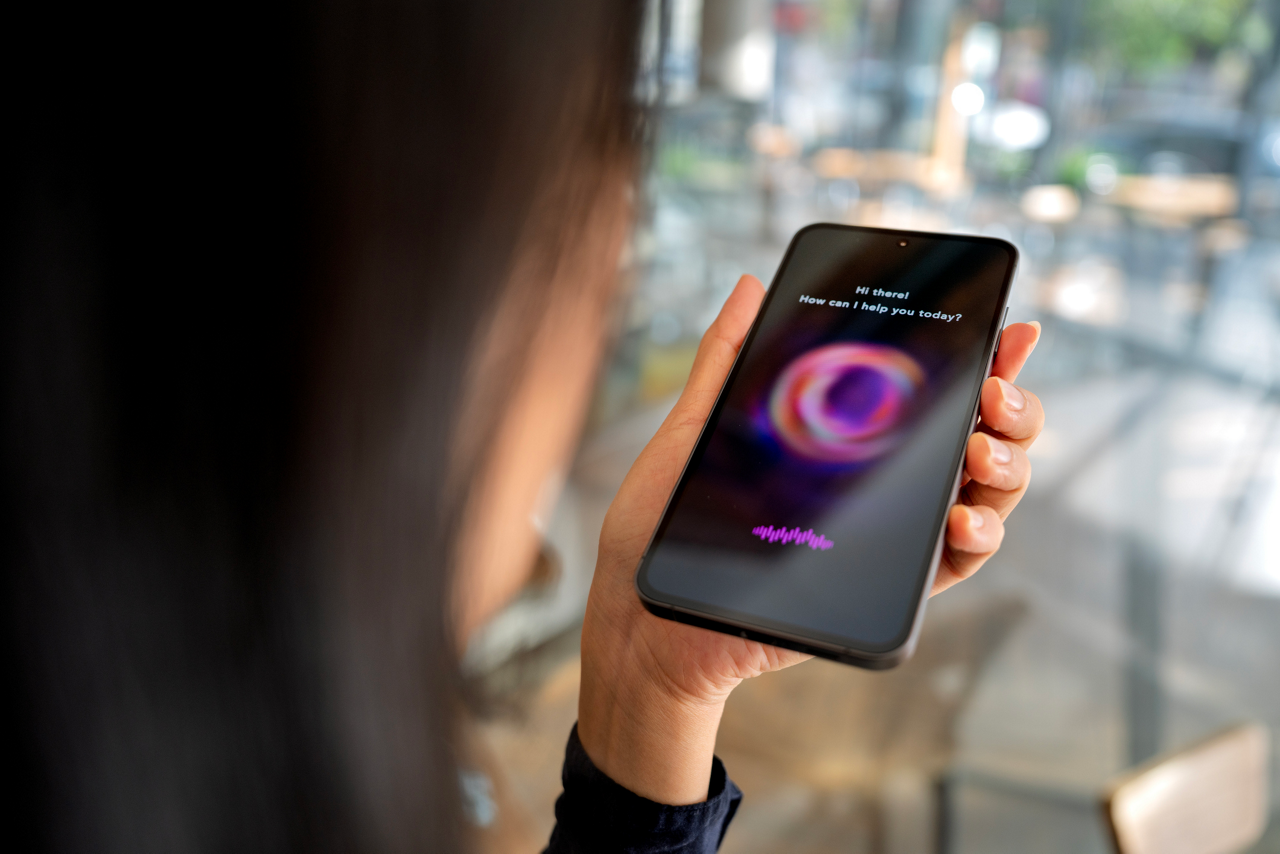 A person interacts with an AI chatbot on a smartphone while sitting outside, using voice assistance for help or information.