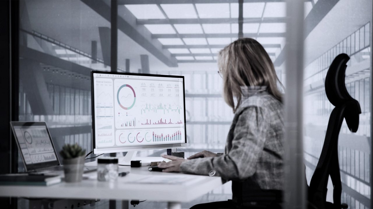 Woman sitting at desk looking at report on computer screen