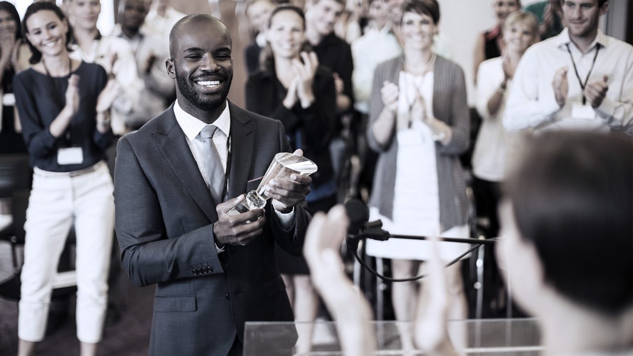 Business professional receiving award with coworkers clapping in background