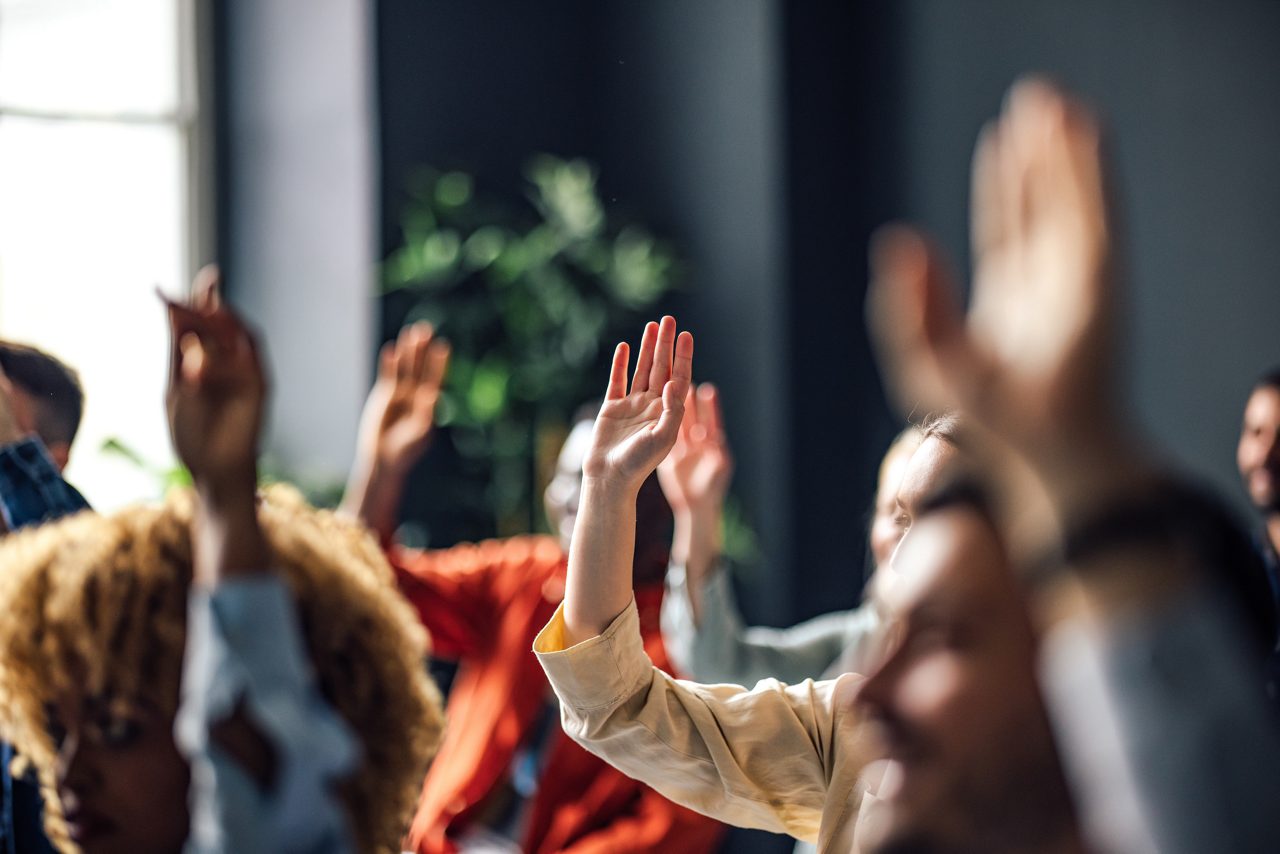 People raise hands in meeting to ask questions