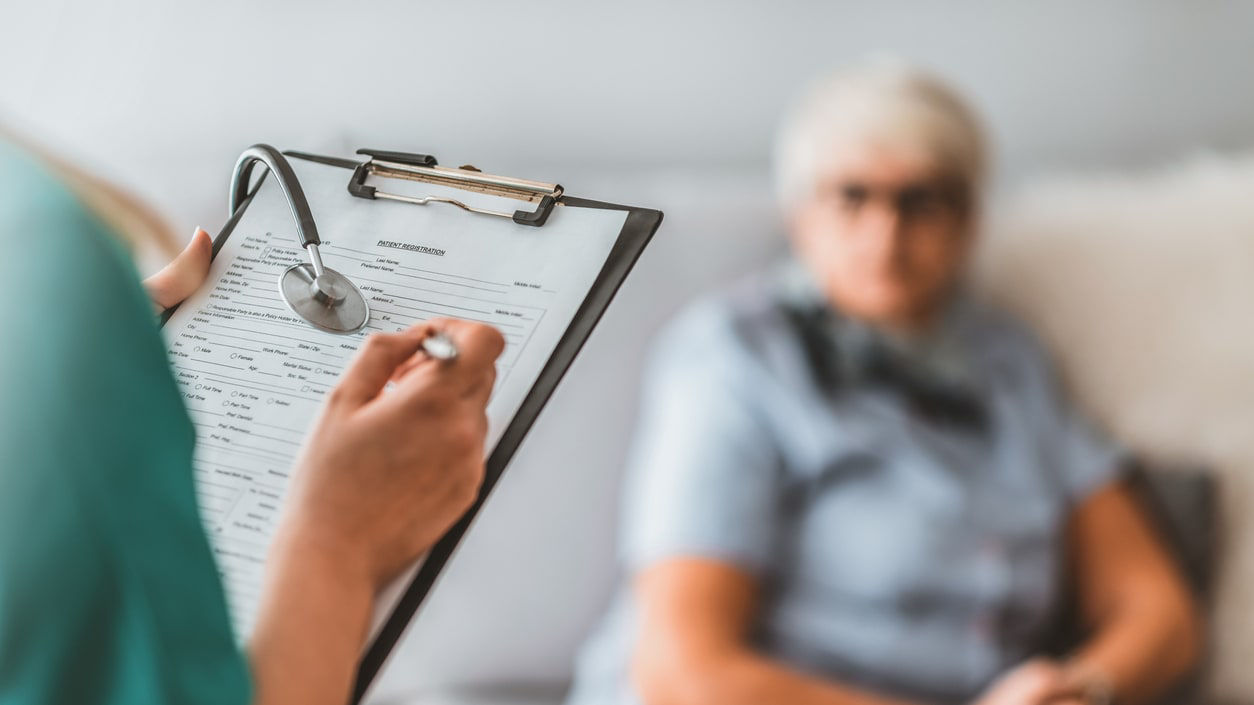 A nurse is holding a clipboard with a stethoscope in front of an elderly woman.