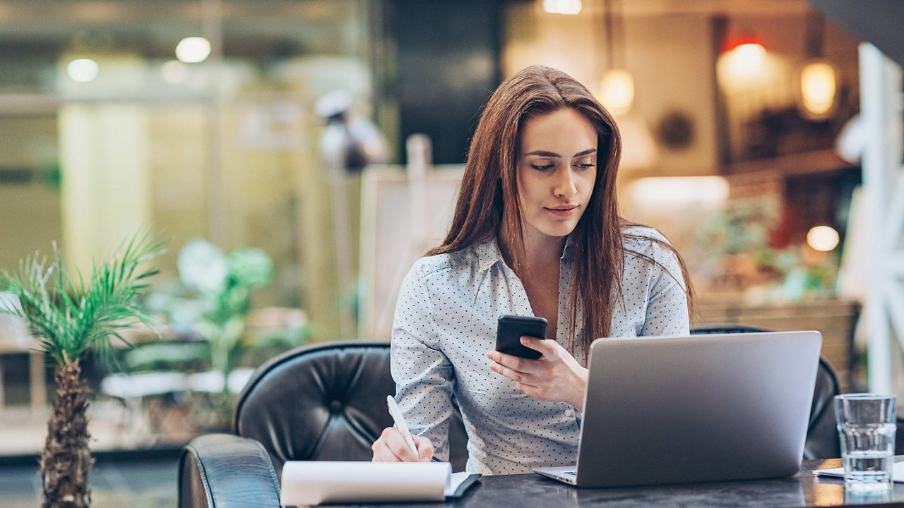 A woman sitting at a table with a laptop and cell phone.