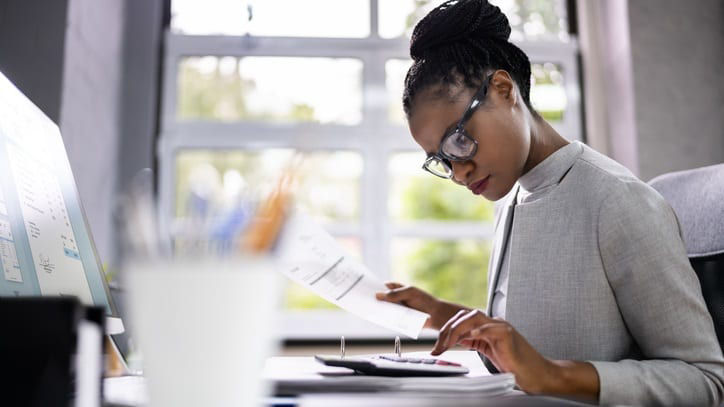 A business woman is working at her desk with a calculator.