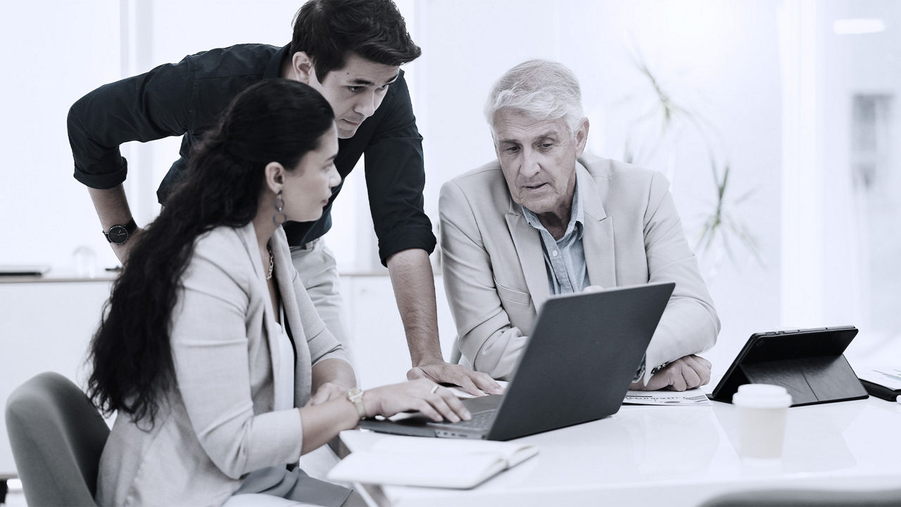 Three workers from various generations collaborate over a laptop.